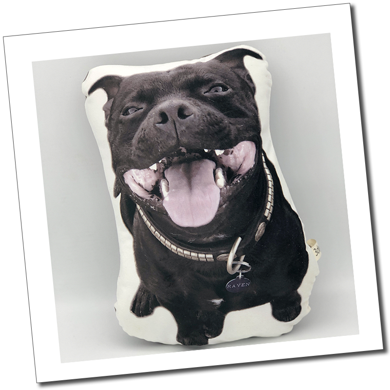 Black Staffordshire bull terrier dog cushion: “Custom cut-out pet cushion featuring a smiling black dog with a collar and name tag.”